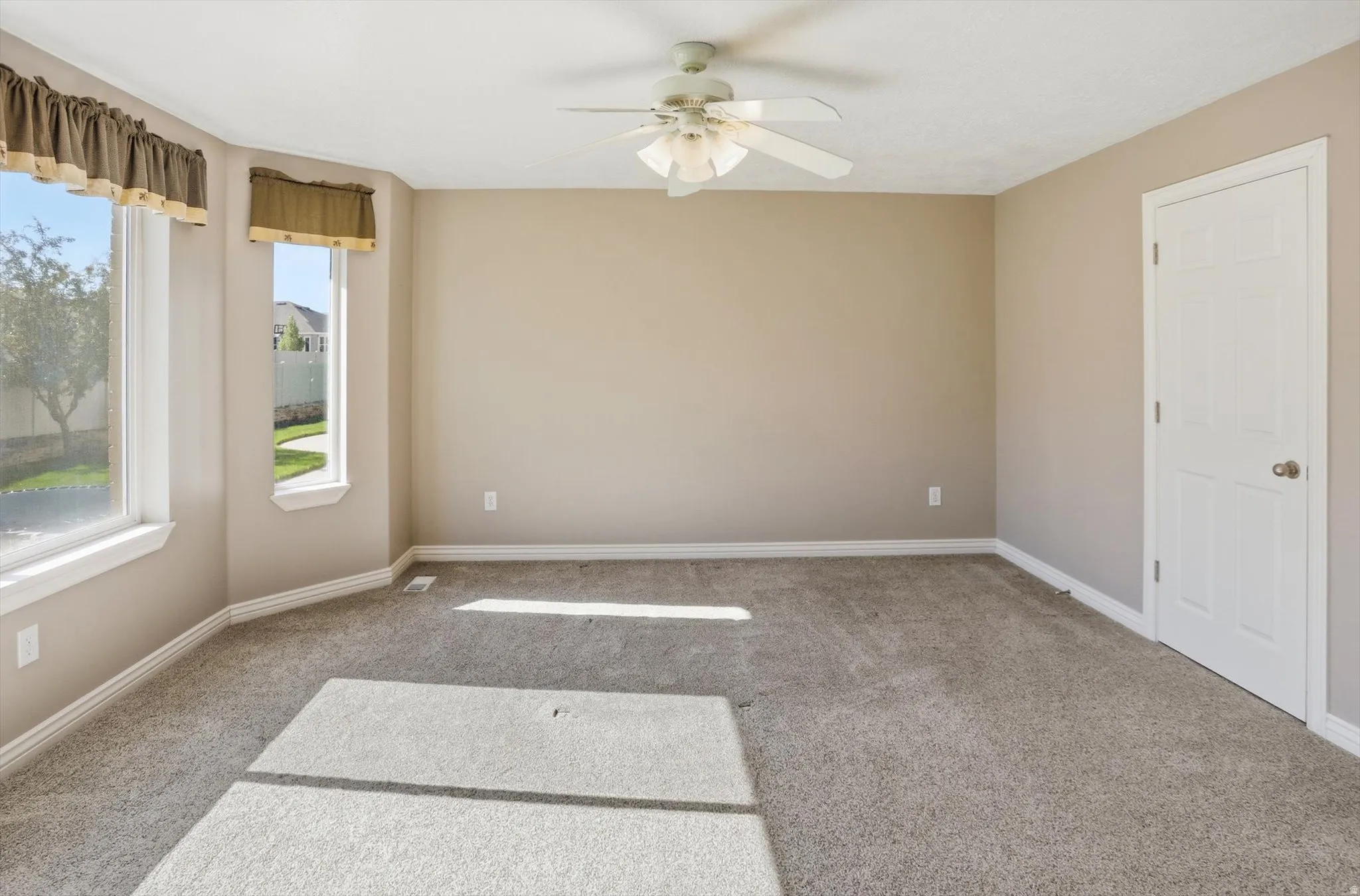 Neutral-toned room featuring a bay window, ceiling fan, plush carpeting, and white trim