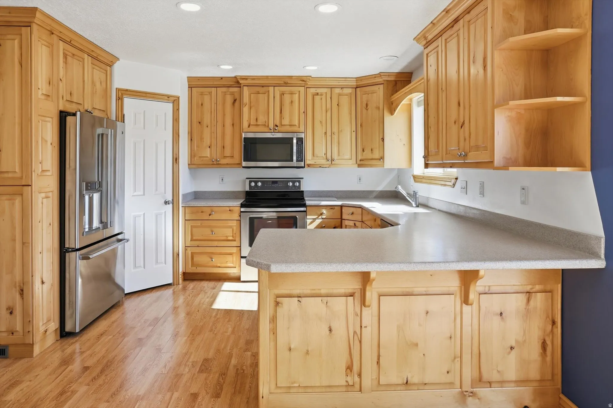 Spacious kitchen featuring light wood cabinetry, stone-finish countertops, and stainless steel appliances