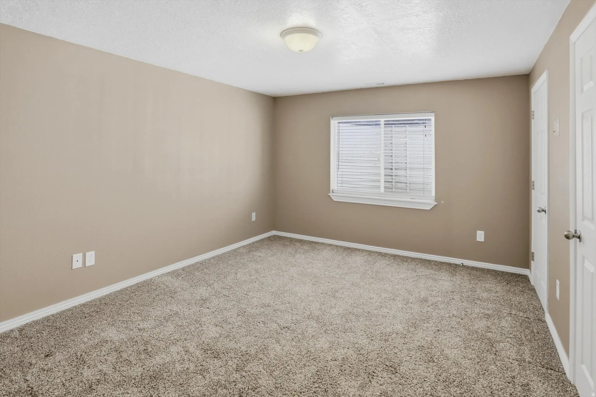 Carpeted interior room featuring neutral wall paint, white trim, a window with blinds, and white paneled doors