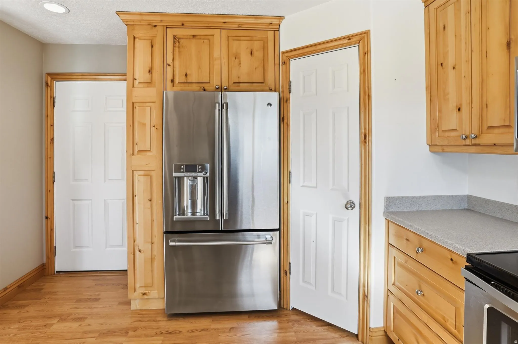 Stainless steel French door refrigerator integrated into custom wood cabinetry, featuring wood-finish flooring, white paneled doors, and grey speckled countertops
