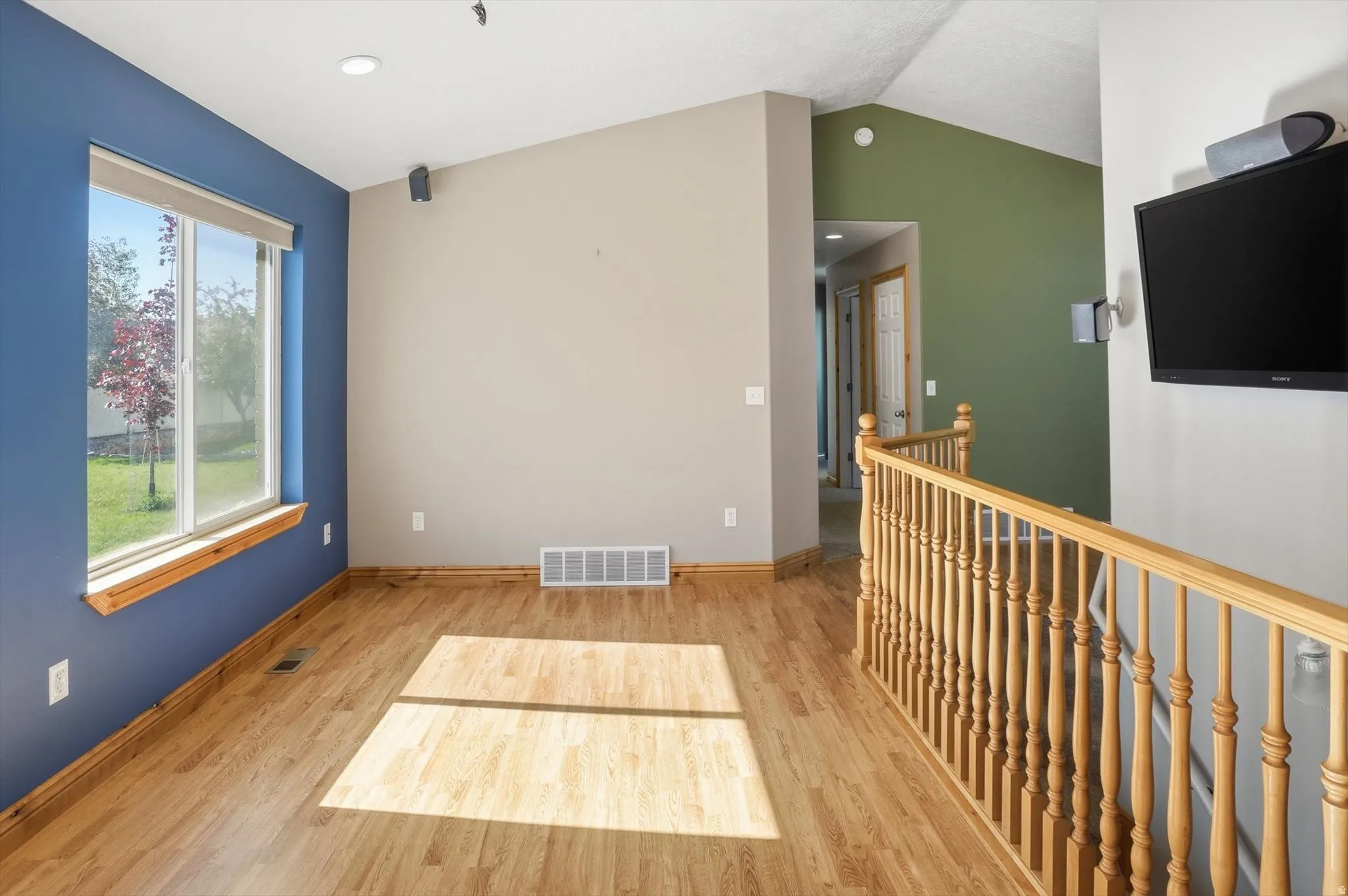 Wood-finish flooring throughout, featuring a large window with a wood sill, recessed lighting, and a wood railing