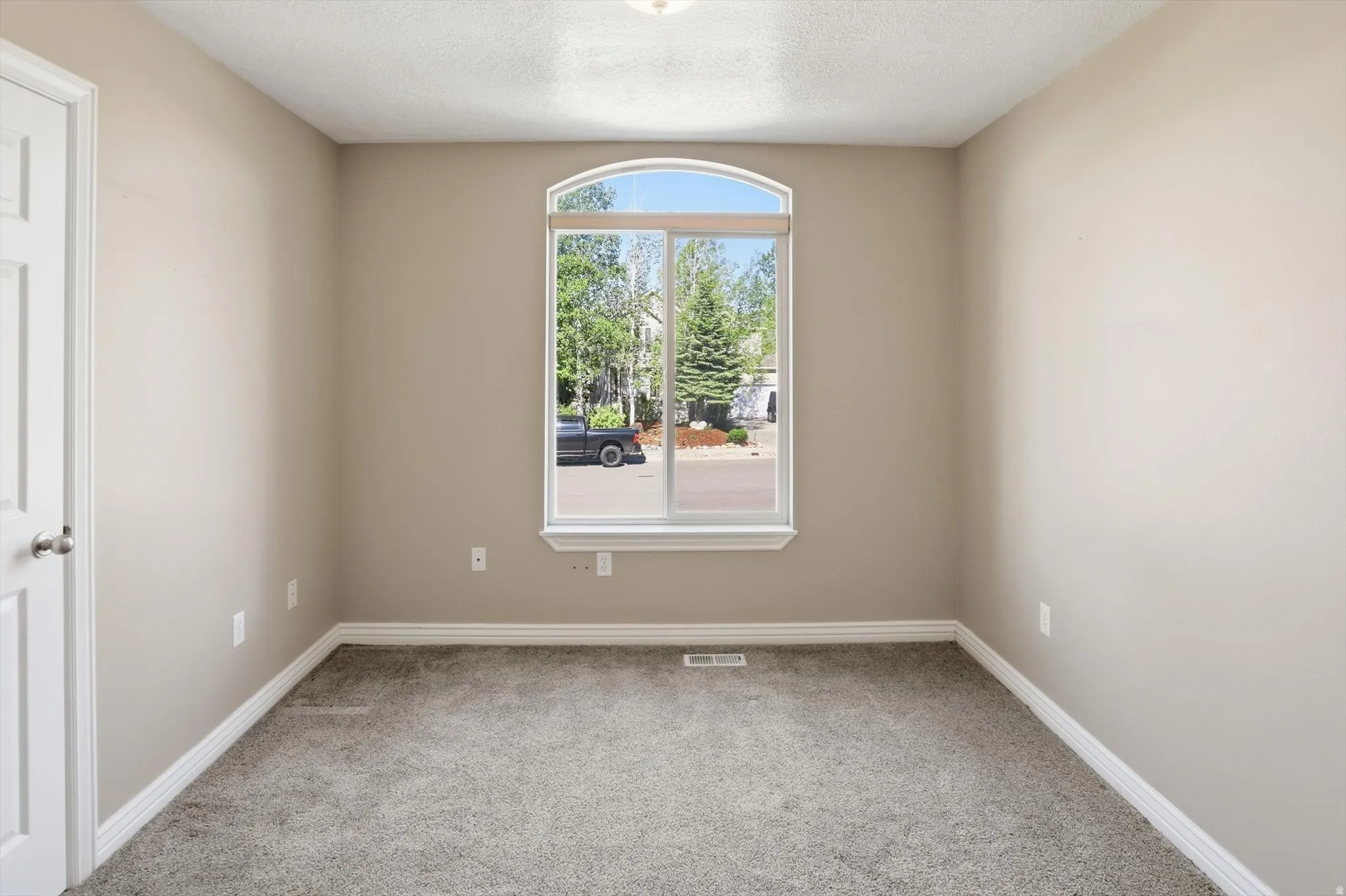 Room featuring an arched window, neutral wall paint, white trim, and gray carpeting