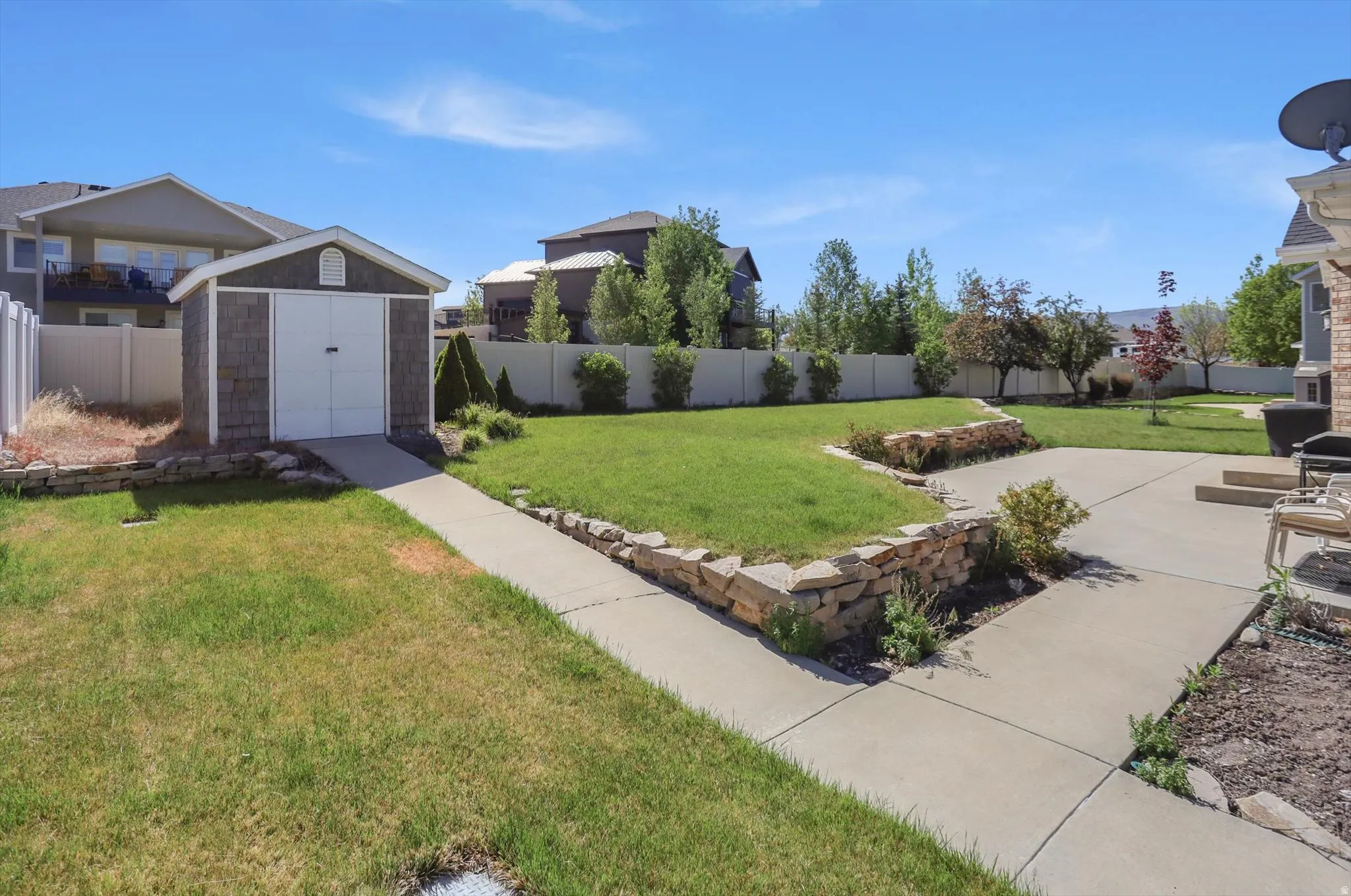 Expansive outdoor space featuring a detached storage shed with a ramp, concrete pathways, a stone retaining wall, and a large grass lawn