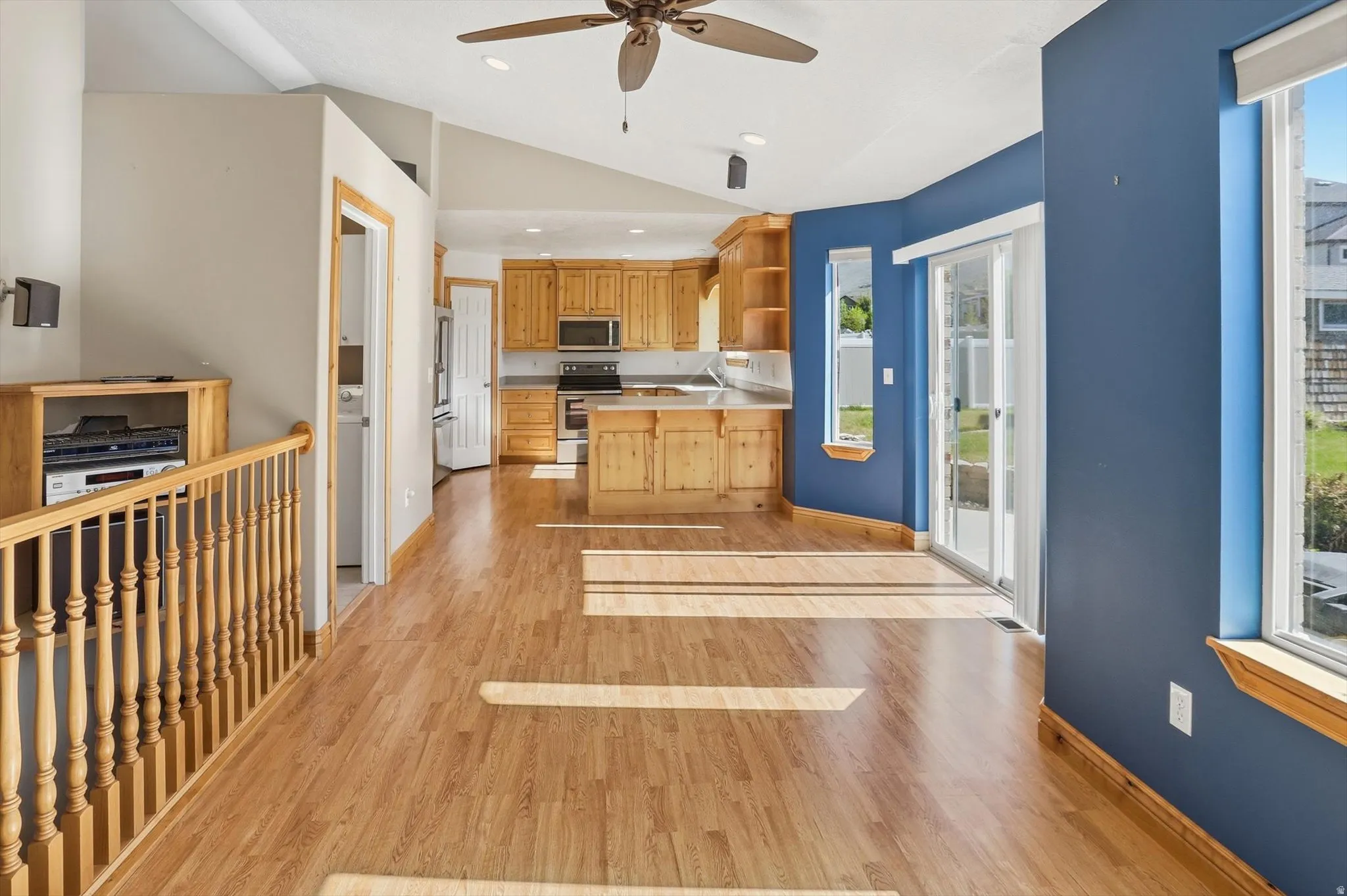 Spacious open-concept living area featuring wood-finish flooring, vaulted ceilings, and a ceiling fan