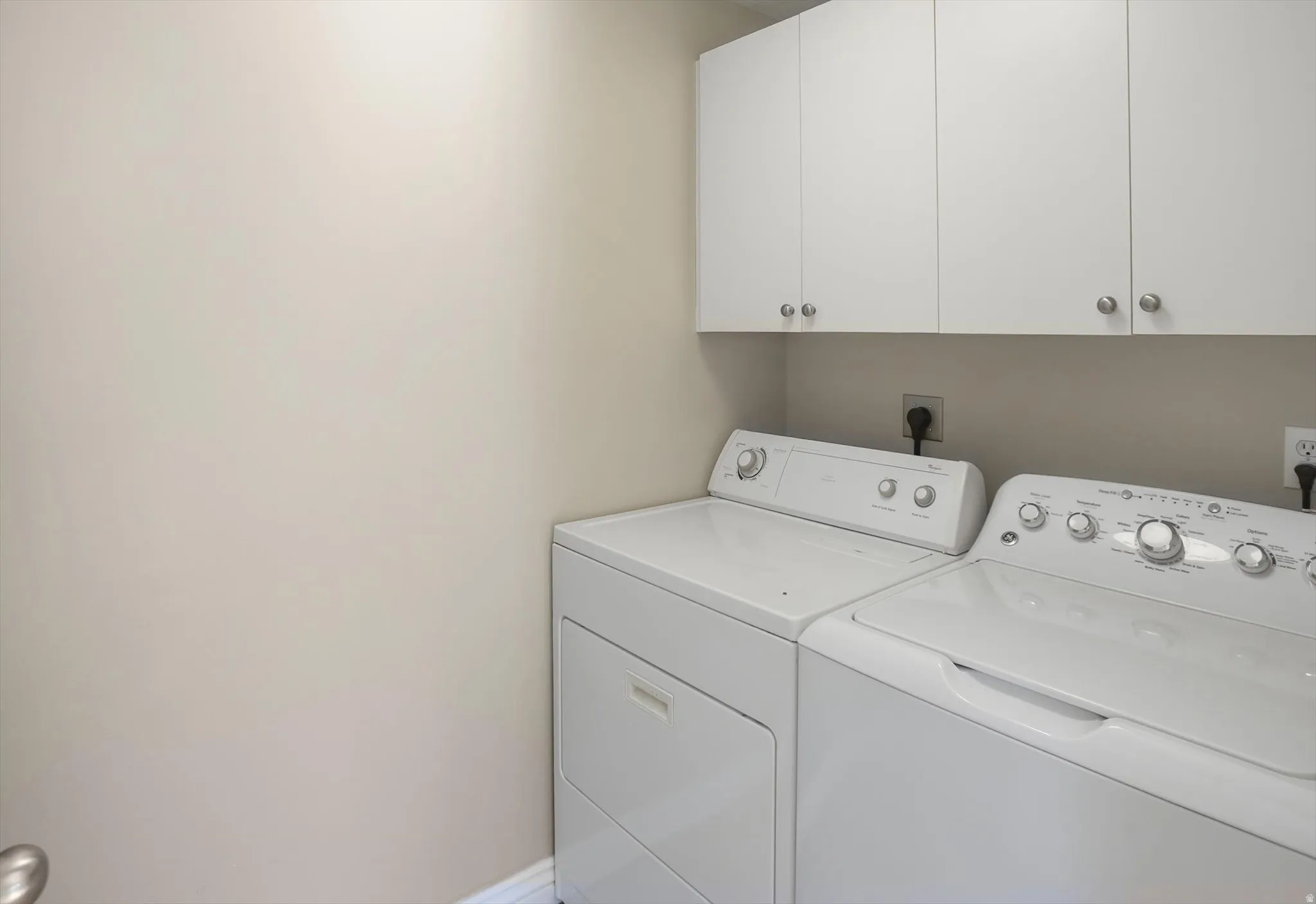 Dedicated laundry area featuring upper white cabinetry with brushed nickel hardware