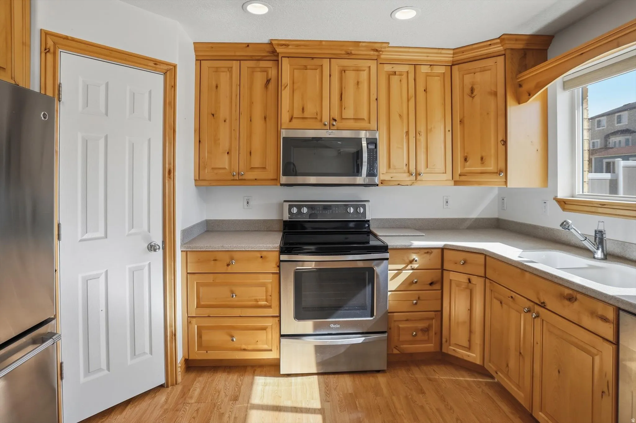 Kitchen featuring wood-finish cabinetry, stainless steel appliances, light-toned countertops, a window above the sink, and recessed lighting