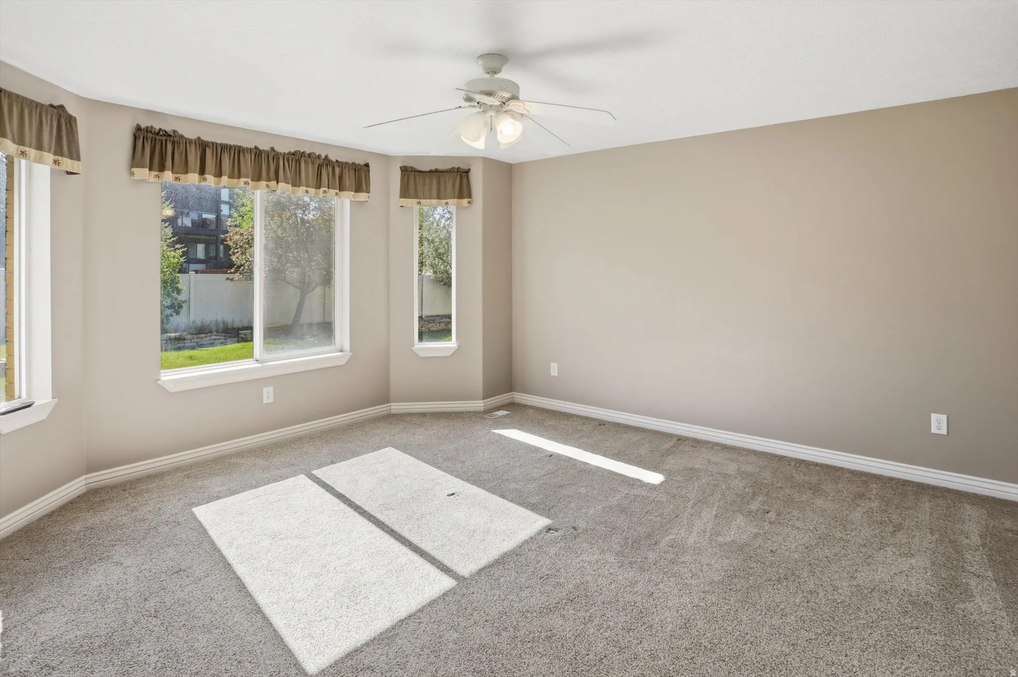 Neutral-toned room featuring a bay window with multiple panes, carpet flooring, and a ceiling fan with integrated lighting