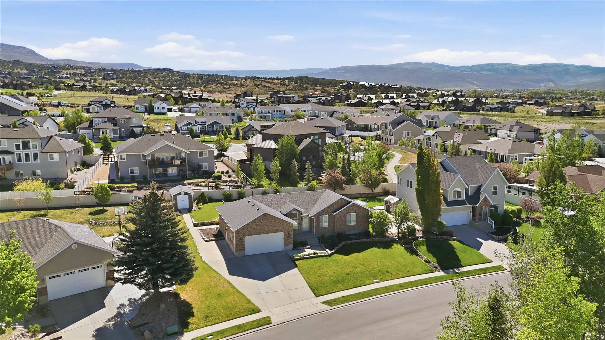 Residential neighborhood with varied architectural styles, mature trees, and mountainous terrain in the distance