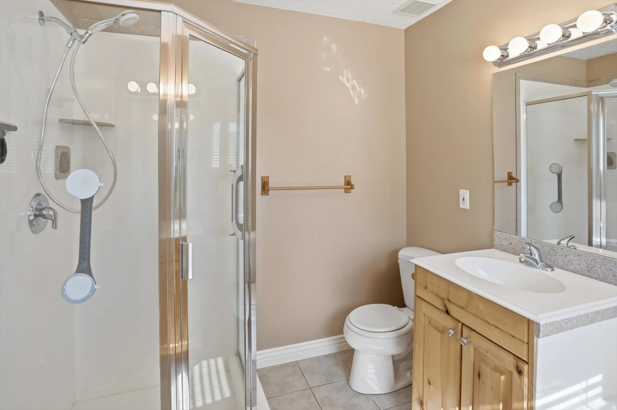 Bathroom featuring a clear glass shower enclosure, a single vanity with a light wood-finish cabinet, a built-in sink, and a speckled countertop