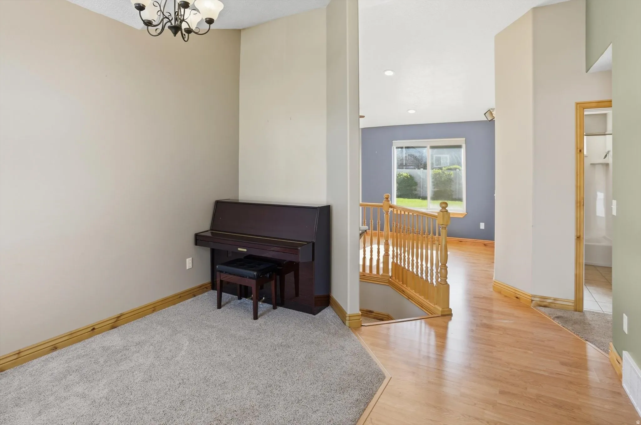 Carpeted area with a decorative chandelier, featuring a hardwood flooring entryway and a wooden staircase with balusters