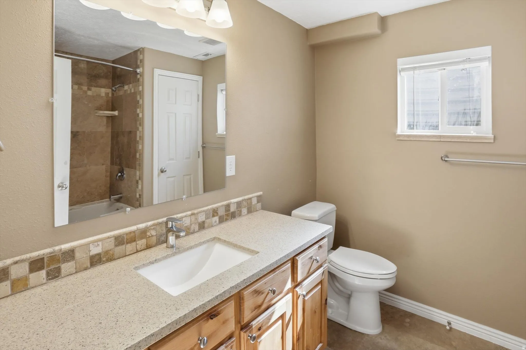 Bathroom featuring a light-toned vanity with an integrated sink, a tiled backsplash, and a large wall-mounted mirror