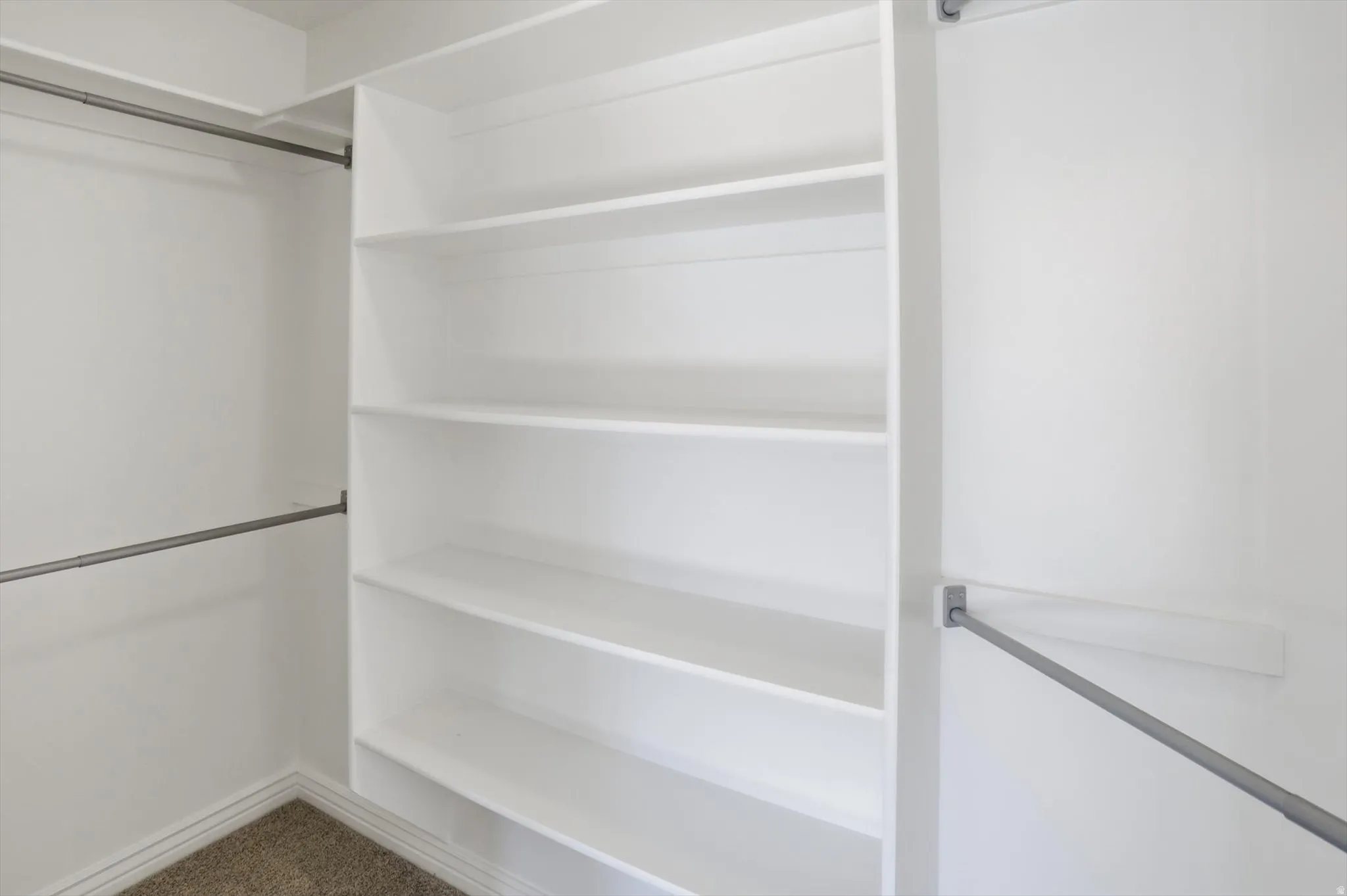 White built-in shelving with multiple storage levels, featuring metal hanging rods and carpet flooring