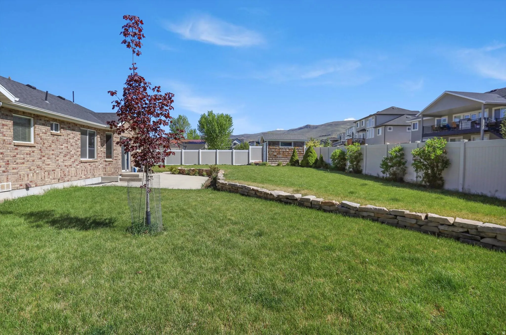 Expansive backyard featuring a tiered lawn, stone retaining wall, and a concrete patio
