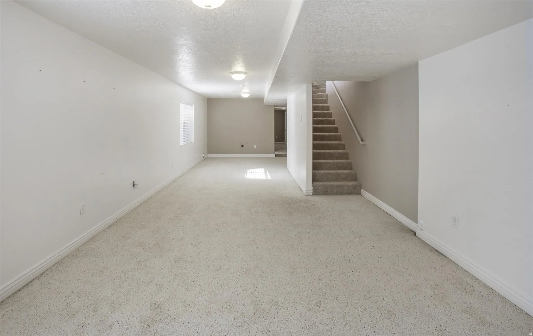 Expansive carpeted room featuring recessed lighting, a neutral color palette, a rectangular window, and a staircase with a handrail