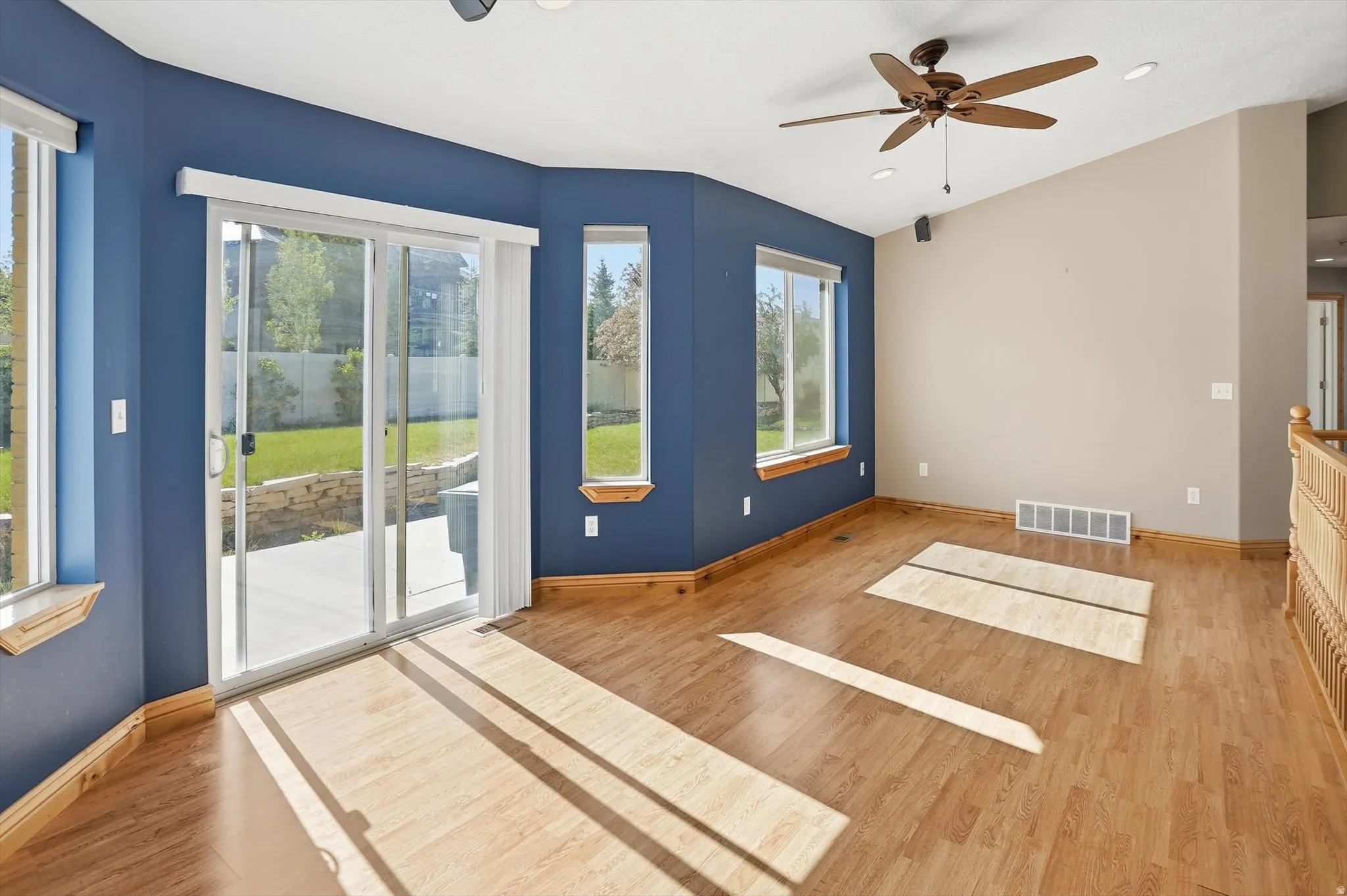 Spacious room featuring wood-finish flooring and a vaulted ceiling with a built-in ceiling fan