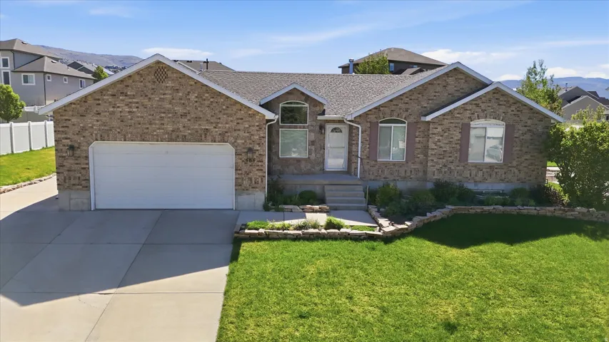 Brick exterior with a peaked roofline, front-facing two-car garage, established front landscaping, concrete driveway, and a front entrance featuring steps and an arched transom window