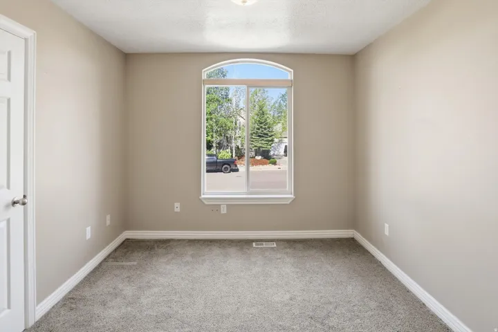 Room featuring an arched window, neutral wall paint, white trim, and gray carpeting