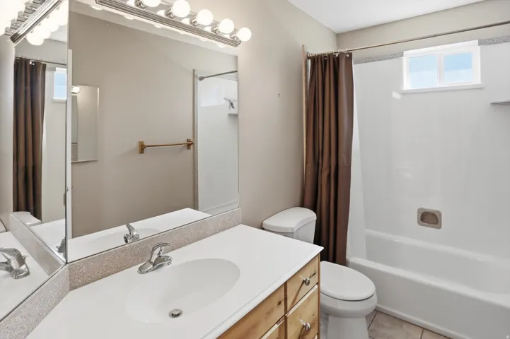 Bathroom featuring a vanity with an integrated sink, a large mirror with a Hollywood-style light fixture, a toilet, and a bathtub/shower combination with an opaque window