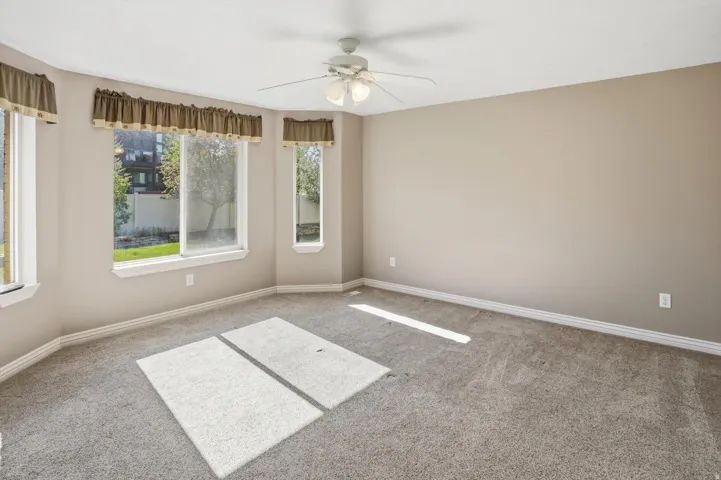 Neutral-toned room featuring a bay window with multiple panes, carpet flooring, and a ceiling fan with integrated lighting