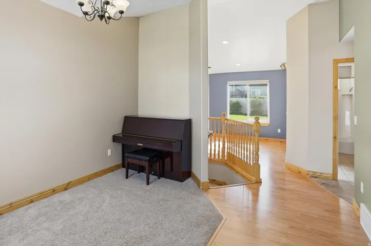 Carpeted area with a decorative chandelier, featuring a hardwood flooring entryway and a wooden staircase with balusters
