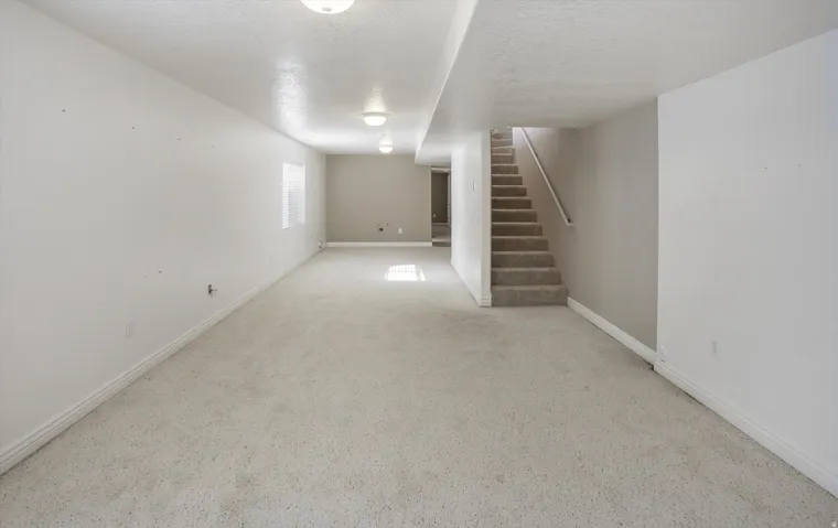 Expansive carpeted room featuring recessed lighting, a neutral color palette, a rectangular window, and a staircase with a handrail