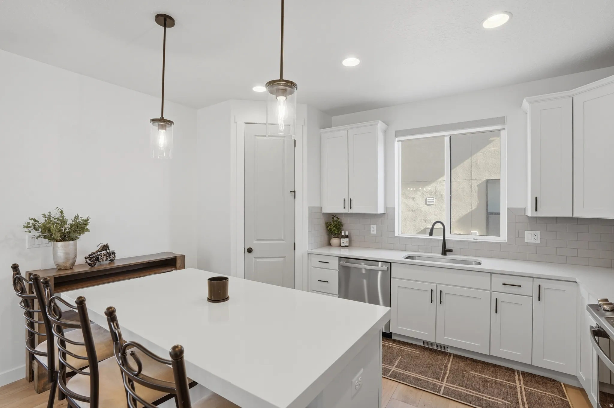 Modern kitchen featuring a large central island with solid surface countertops, white shaker cabinetry, stainless steel appliances, a matte black faucet, and pendant lighting