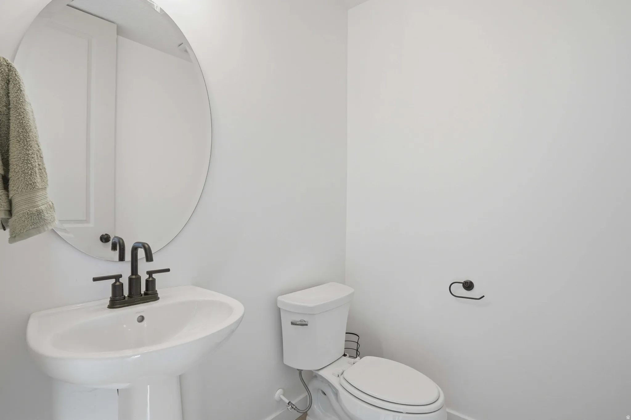 Pedestal sink with matte black hardware, oval mirror, and white toilet