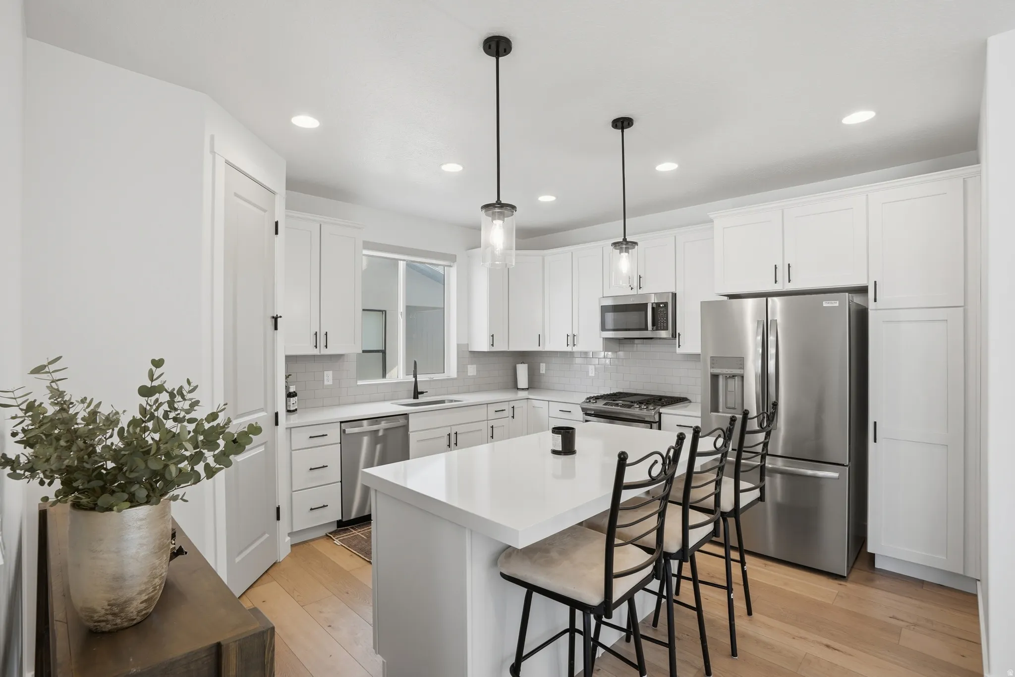 Modern kitchen featuring a central island with white countertop, stainless steel appliances, white shaker cabinetry, and wood-finish flooring