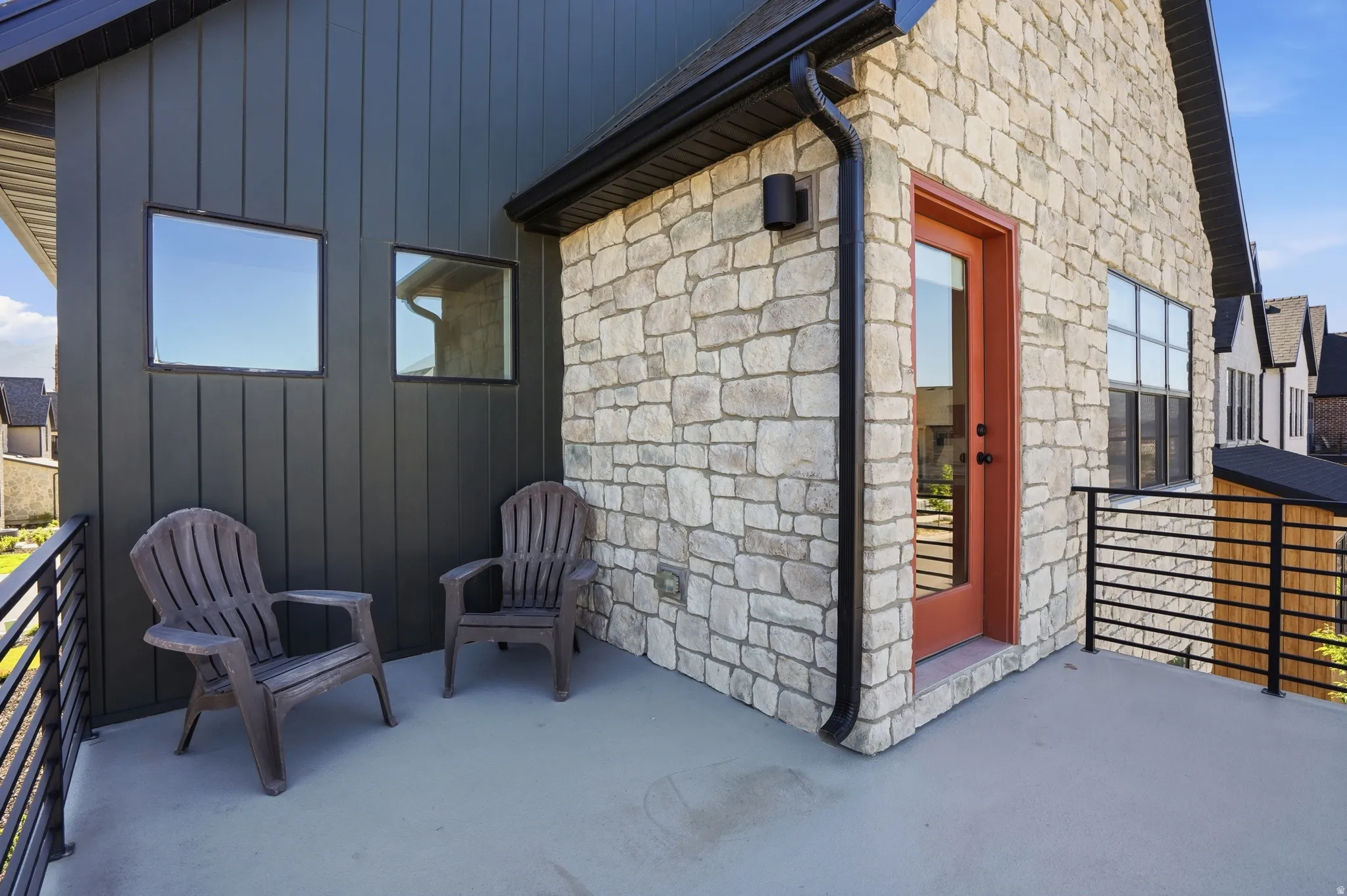 Exterior balcony featuring a smooth concrete surface, black metal railing, and a red-orange door