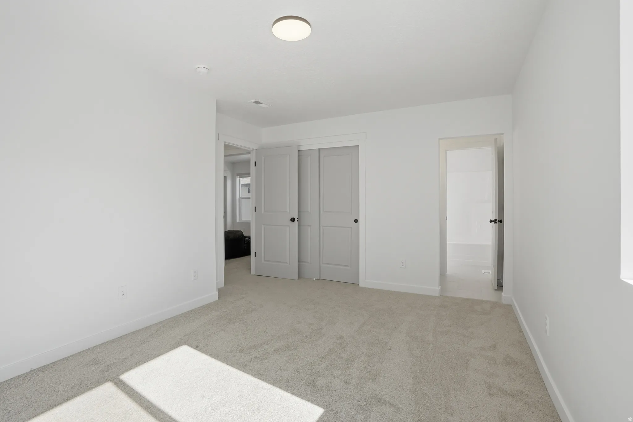 Spacious room featuring light gray carpeting, white painted walls, and a contemporary ceiling light fixture