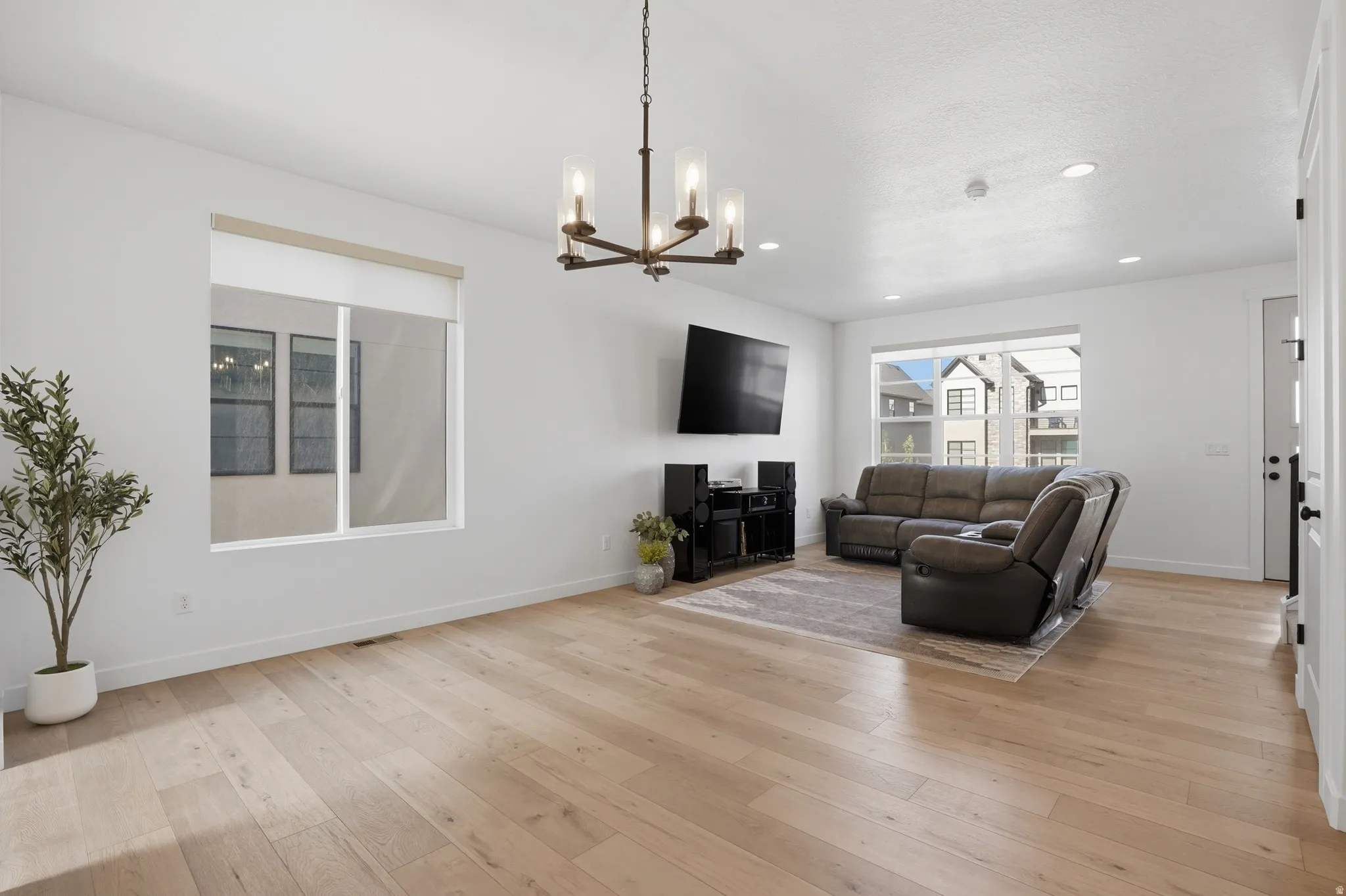 Bright living area featuring light wood-finish flooring, recessed lighting, and a modern bronze chandelier