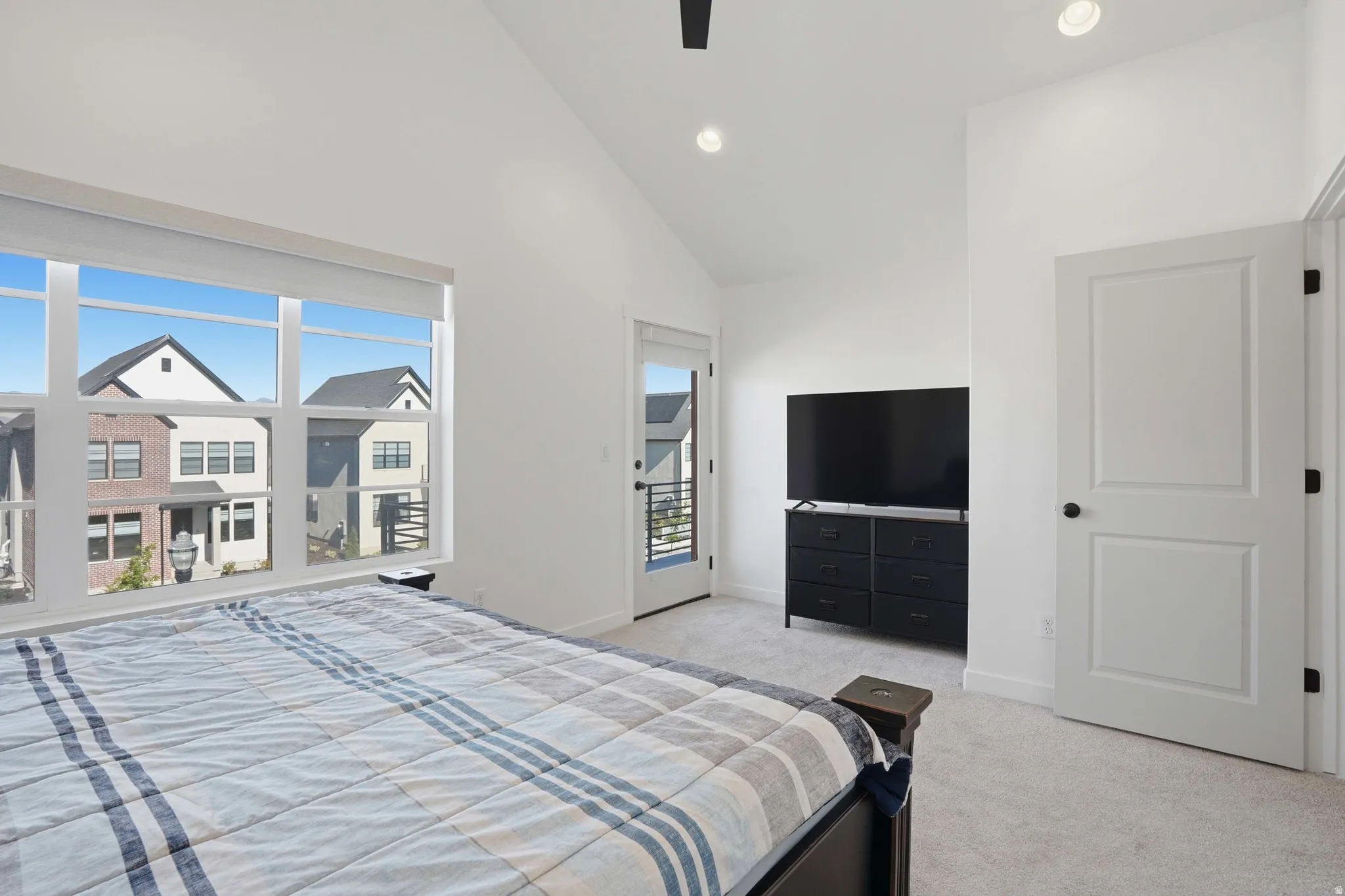 Carpeted room featuring a large window, a balcony door, vaulted ceilings, and recessed lighting