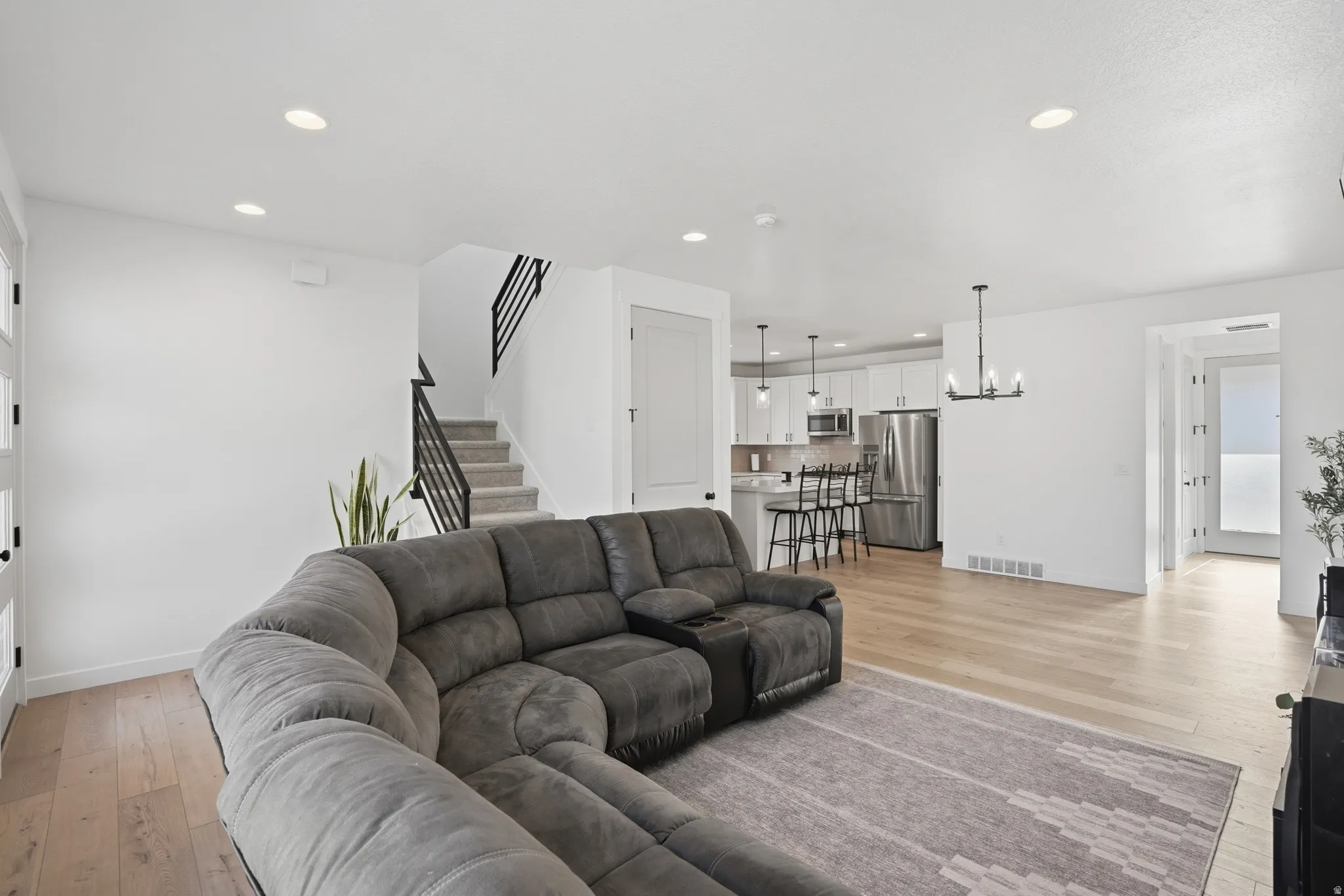 Spacious open-concept living area featuring light wood-finish flooring, recessed lighting, and a contemporary black metal staircase railing