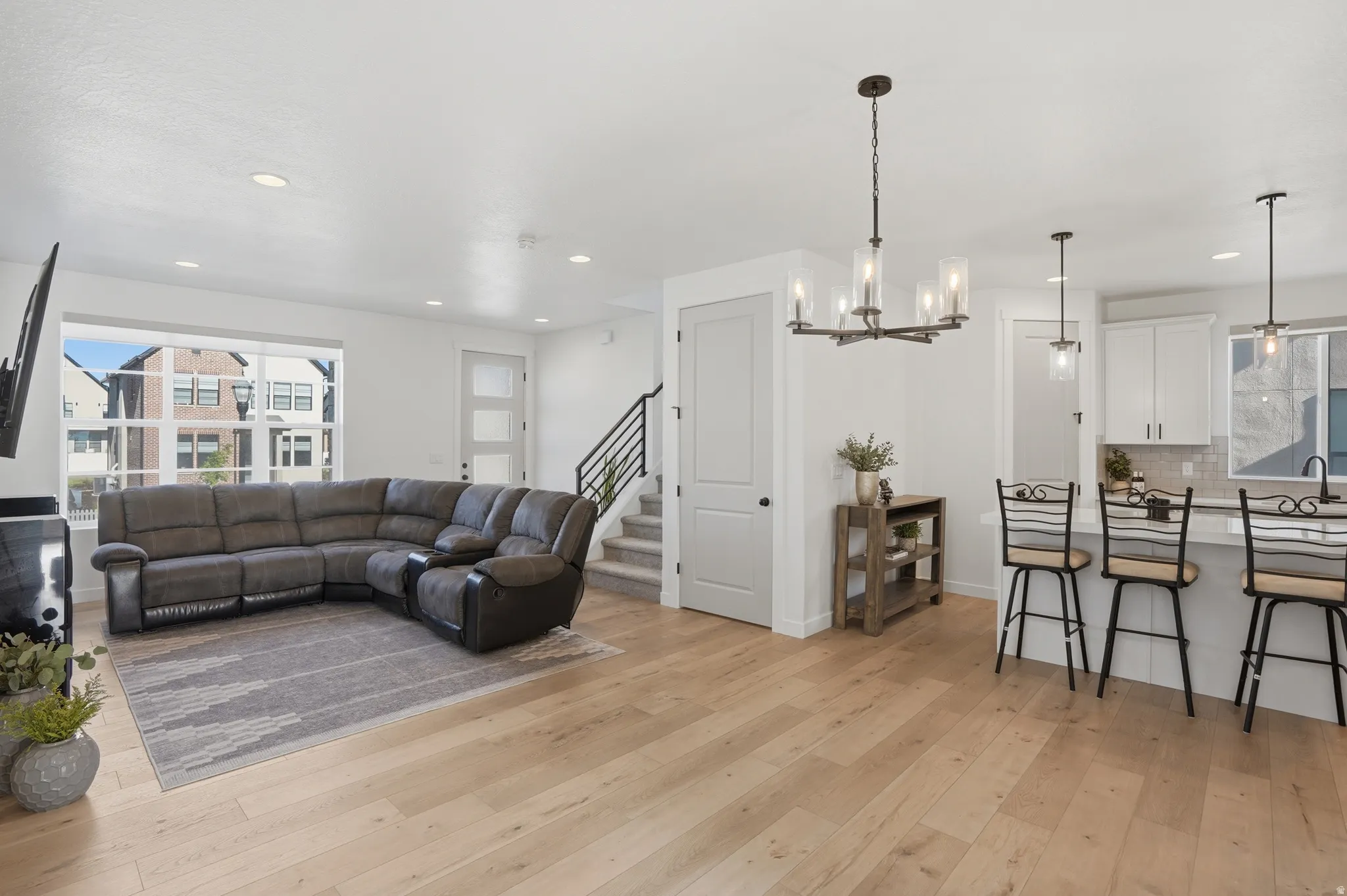 Bright open-concept living space featuring light wood-finish flooring, recessed lighting, and a modern chandelier