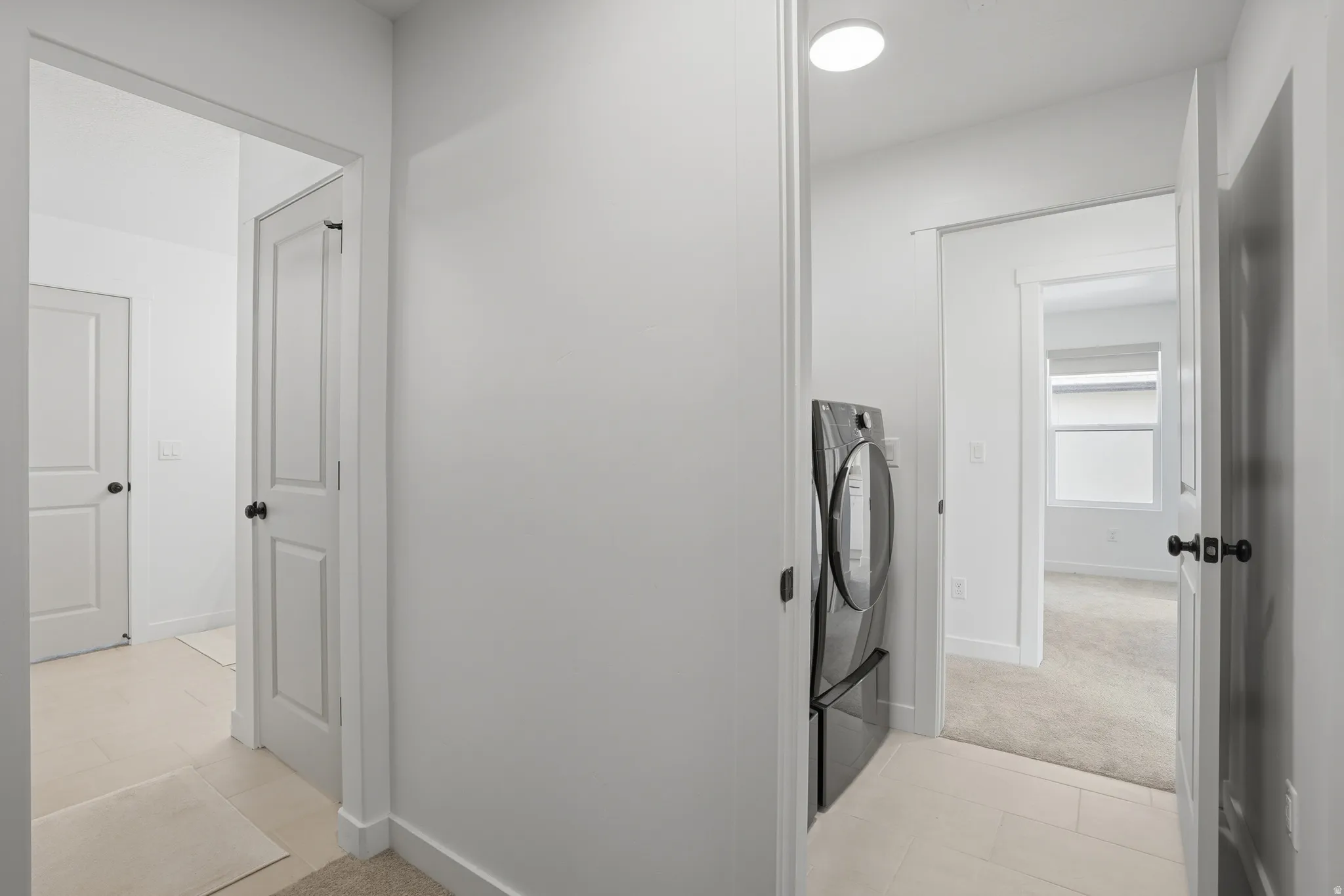 Hallway featuring light-toned tile flooring, recessed ceiling lighting, and a modern front-load washer