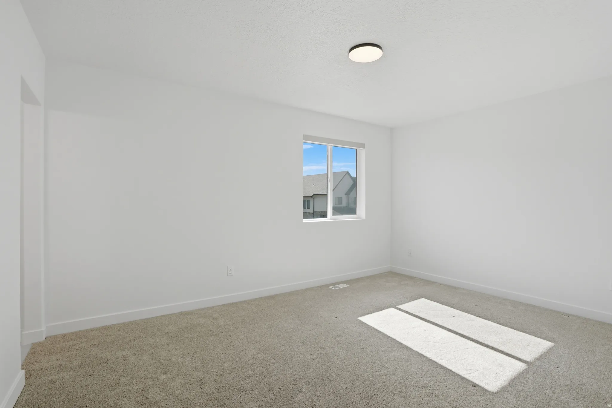 Carpeted room featuring a single window with white trim, a flush-mount ceiling light, and white baseboards