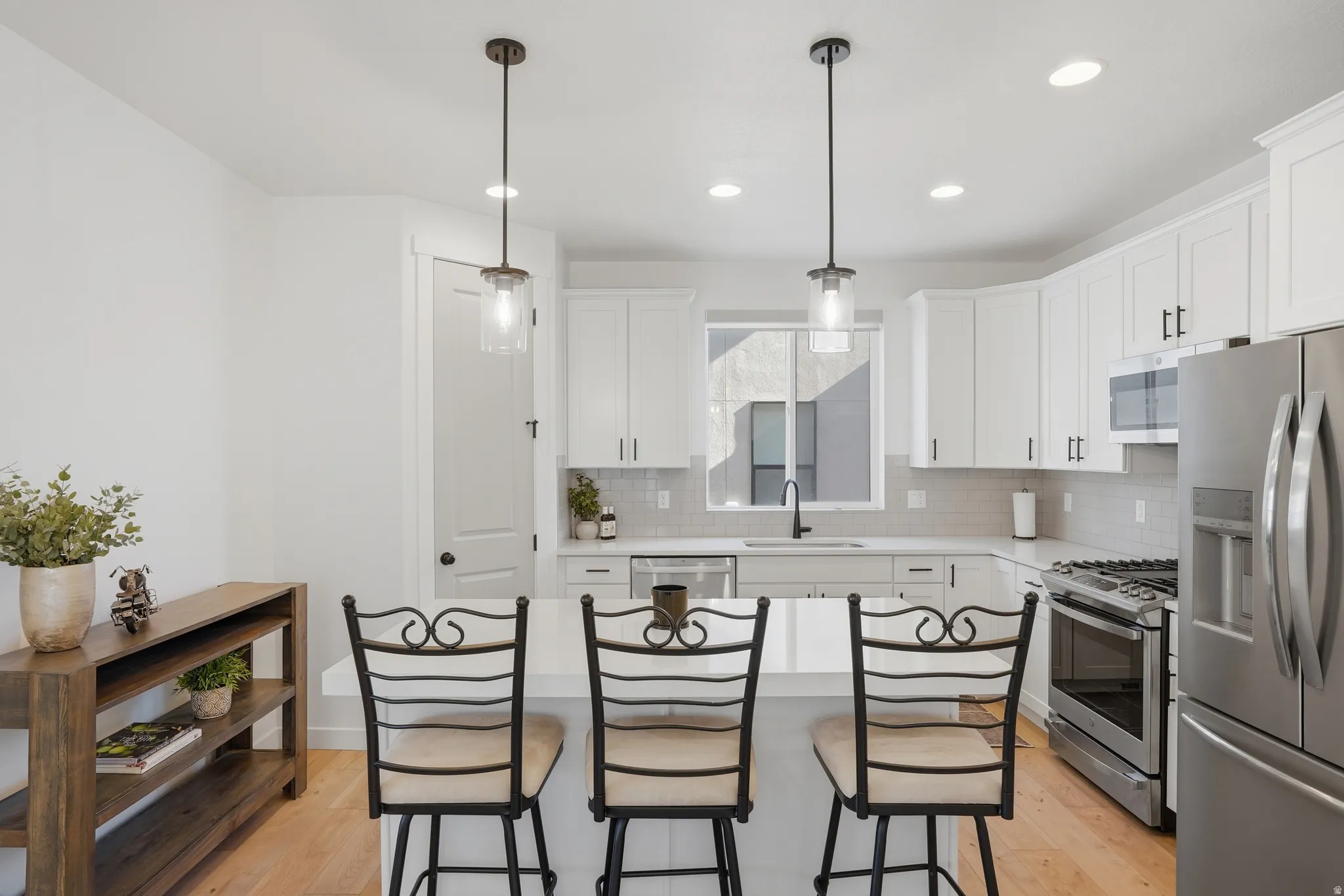 Kitchen featuring light wood-finish flooring, white cabinetry, stainless steel appliances, and a central island with pendant lighting