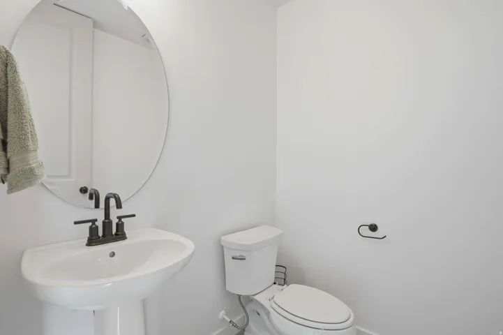 Pedestal sink with matte black hardware, oval mirror, and white toilet