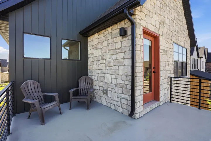 Exterior balcony featuring a smooth concrete surface, black metal railing, and a red-orange door
