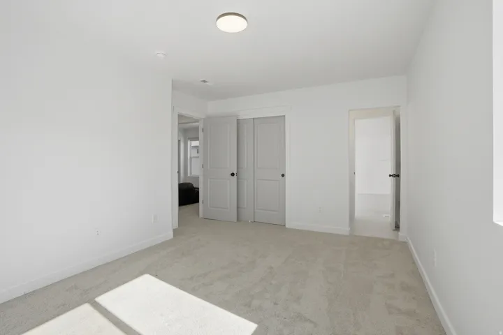 Spacious room featuring light gray carpeting, white painted walls, and a contemporary ceiling light fixture