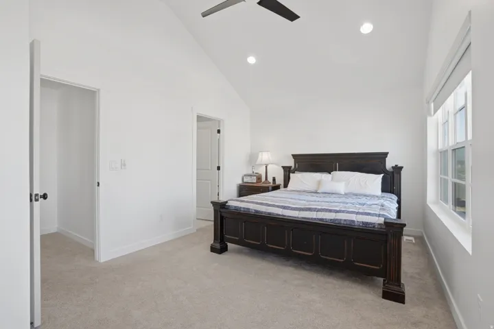 Vaulted ceiling bedroom with light-colored carpeting and bright white walls