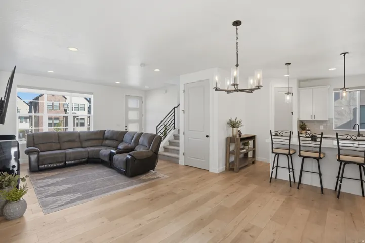 Bright open-concept living space featuring light wood-finish flooring, recessed lighting, and a modern chandelier