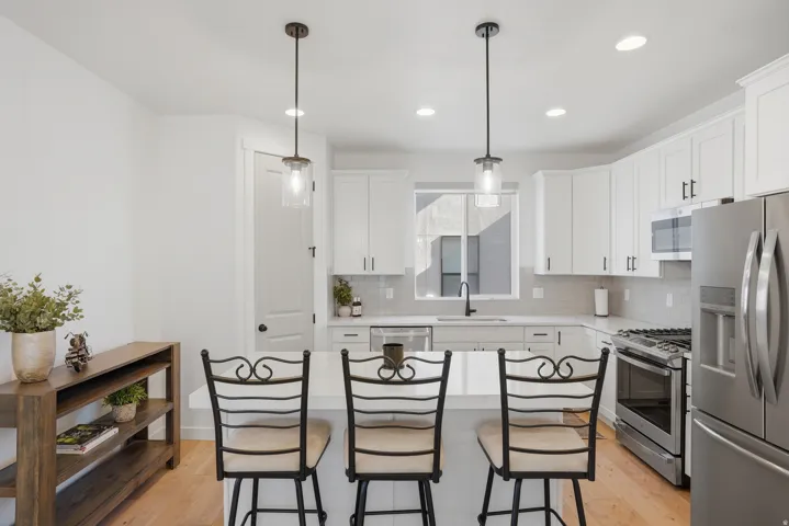 Kitchen featuring light wood-finish flooring, white cabinetry, stainless steel appliances, and a central island with pendant lighting