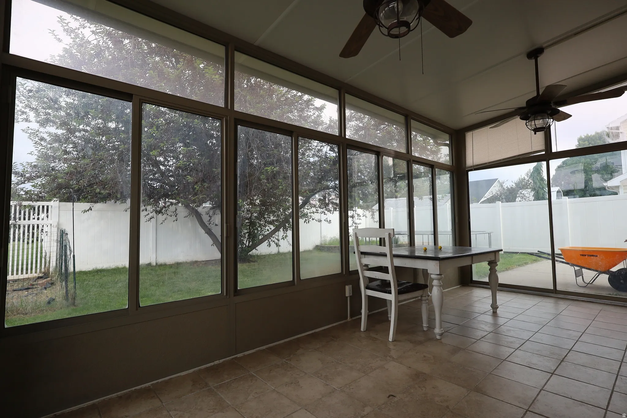 Screened porch featuring extensive window panels, tiled flooring, two ceiling fans, and a white fence enclosing the backyard