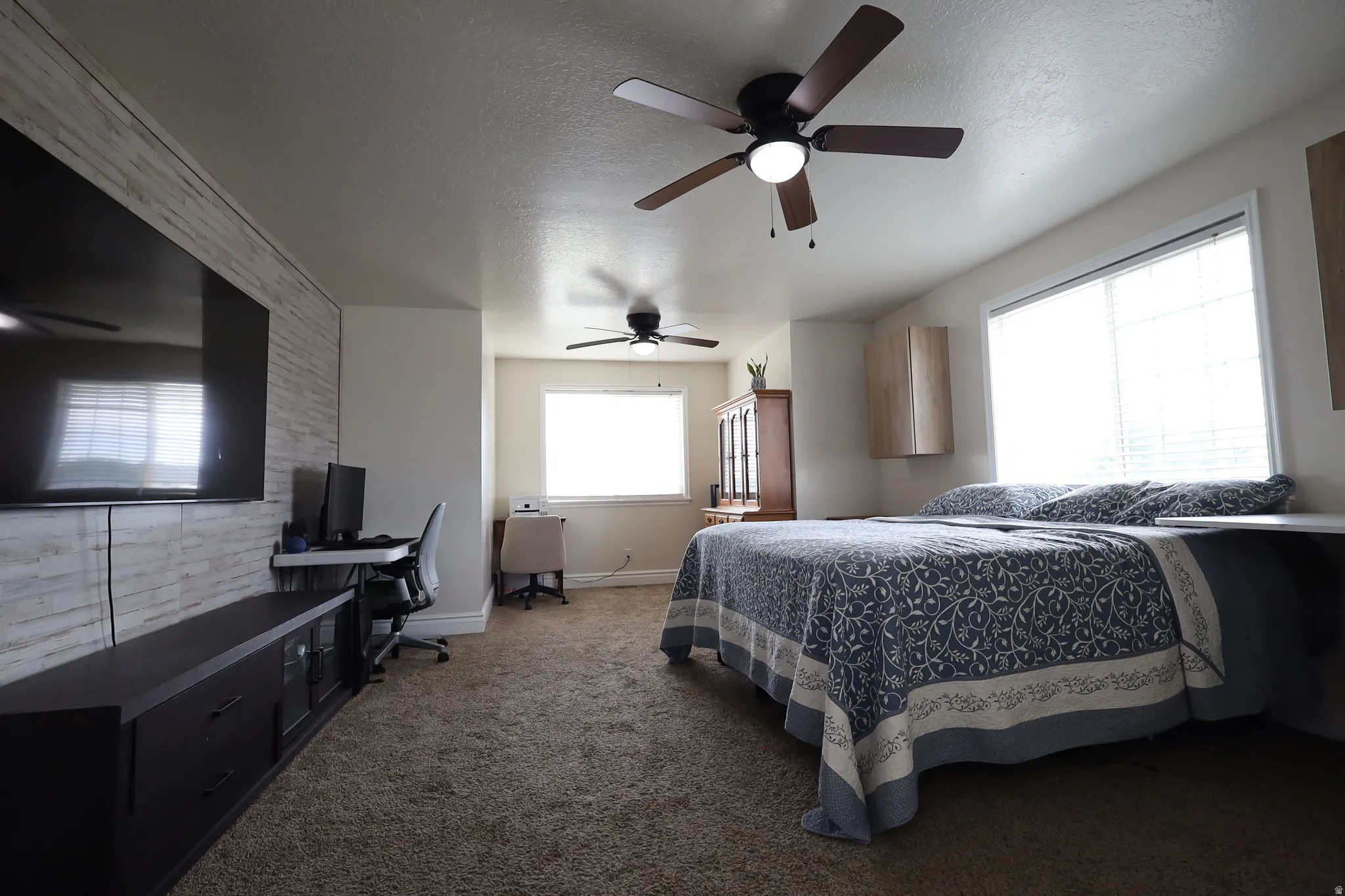 Carpeted room featuring a built-in media wall with wood-finish paneling, two ceiling fans, and multiple windows