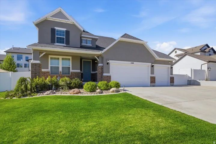 Two-story residence featuring a gray stucco and brick exterior with a multi-car garage and a blue entry door