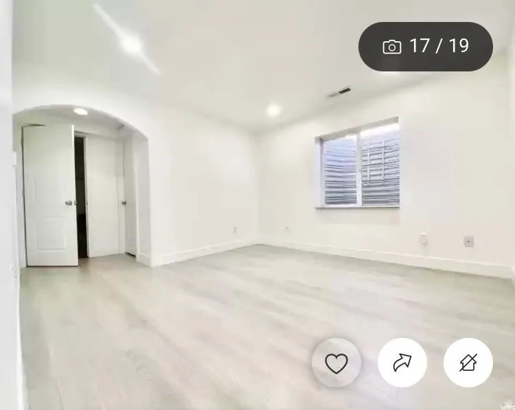 Spacious room featuring light wood-finish flooring, white walls, and a window with blinds