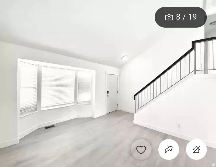 Bright interior space featuring light wood-finish flooring, a bay window with blinds, and a contemporary staircase with black railing