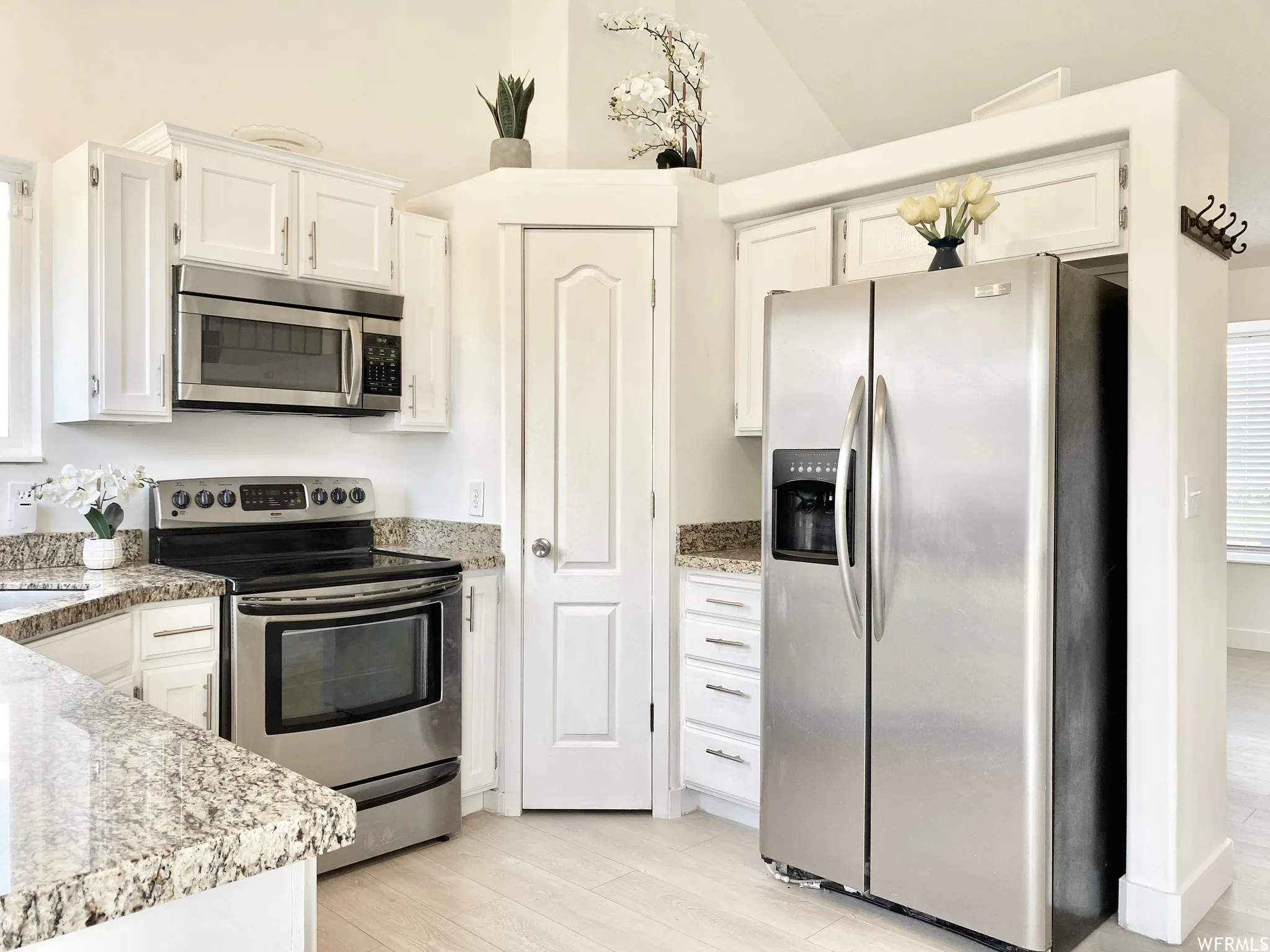 Kitchen featuring light-toned cabinetry, stainless steel appliances, granite-style countertops, and wood-finish flooring