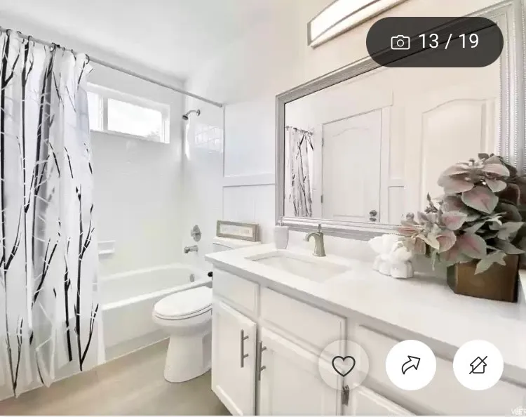 Bright bathroom featuring a white vanity with an integrated sink, a large framed mirror, and a white bathtub with tile surround